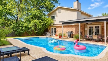Un jardin avec une piscine, des chaises longues et un espace barbecue.