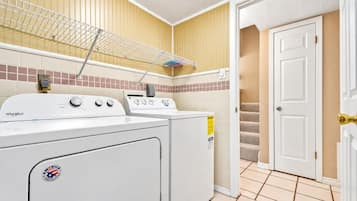 Un lavadero con lavadora y secadora Whirlpool, un tendedero metálico y una puerta que da a una escalera.
