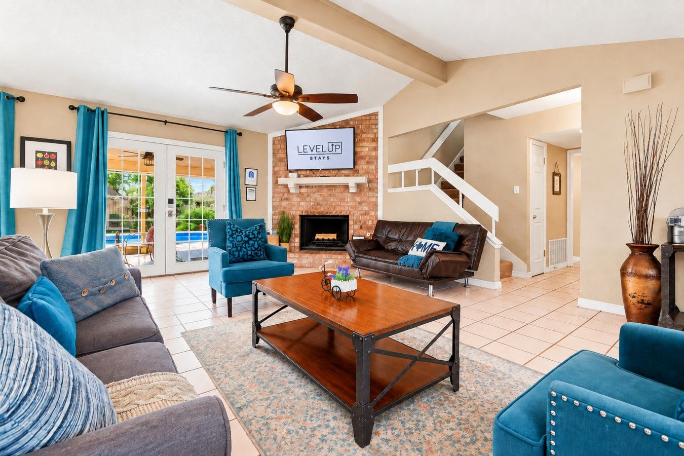 A modern living room with a fireplace, a ceiling fan, and a staircase leading to another level.