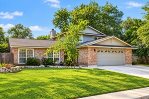 A two-story house with a brick facade, a garage, and a well-maintained lawn. - Swim by Day~Soak by Night~Fenced Yard~Poolside BBQ (San Antonio)