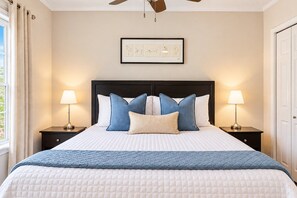 A neatly made bed with a quilted white duvet, a blue quilted throw, and multiple pillows in shades of blue and white. There are two bedside lamps on either side of the bed, and a framed artwork above the bed. - Swim by Day~Soak by Night~Fenced Yard~Poolside BBQ (San Antonio)