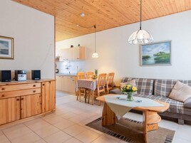 Ein gemütliches Wohnzimmer mit einer Couch, einem Esstisch mit Stühlen, einem Holzschrank und einer Küche im Hintergrund.