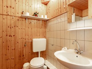 Ein Badezimmer mit Holzwandverkleidung, einer Toilette, einem Waschbecken und einem Spiegel.