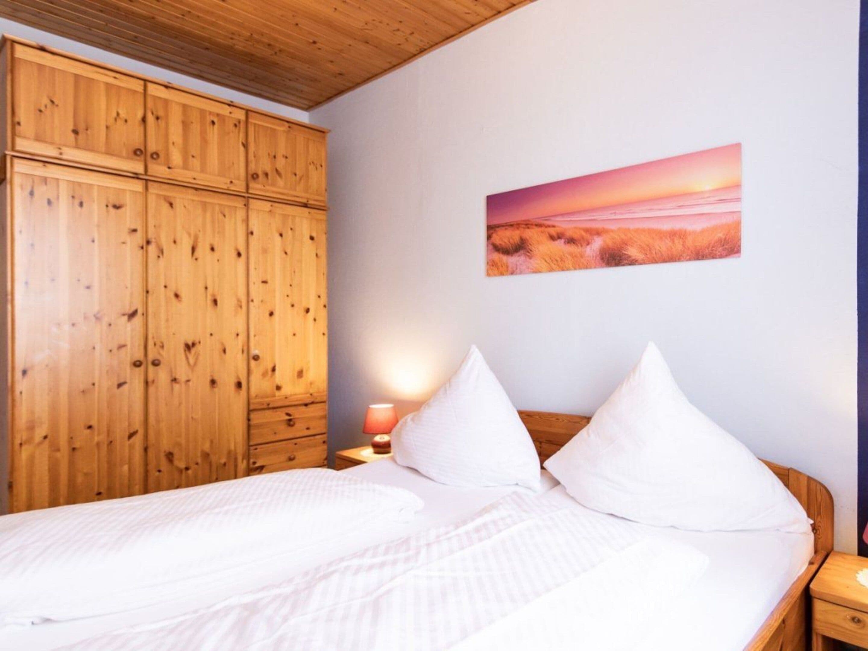Quarto com cama, guarda-roupa de madeira e um quadro na parede.