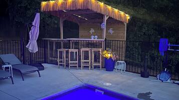 A poolside area with a tiki bar, lounge chairs, and a small pool.