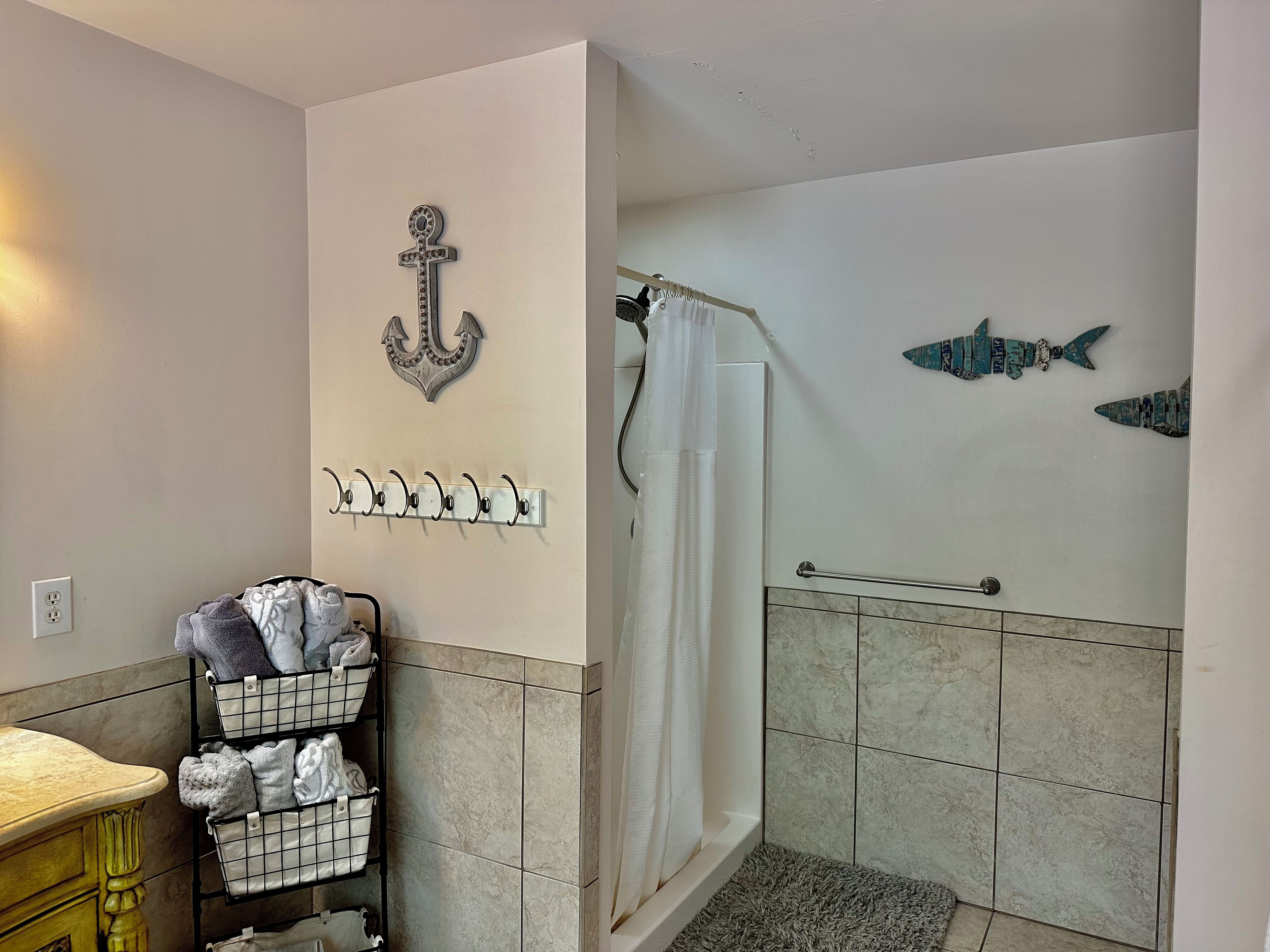 Un baño con ducha, paredes de azulejos, un perchero y un escurridor con toallas.