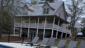Een zwembad met ligbedden, een overdekt terras en een groot huis op de achtergrond.