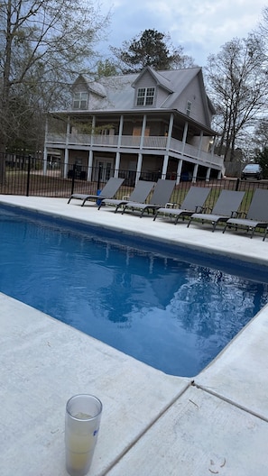A swimming pool with lounge chairs, a covered patio, and a large house in the background. - Perrydise Lakehouse with Pool, Hot Tub & Sunset Views (Shelby)