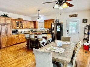 Una cocina con armarios de madera, un refrigerador y un comedor con mesa y sillas.