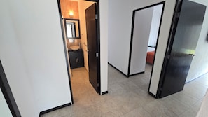 A corridor with a bathroom and a bed visible through an open door. - La reserva suites (Santiago de Querétaro)