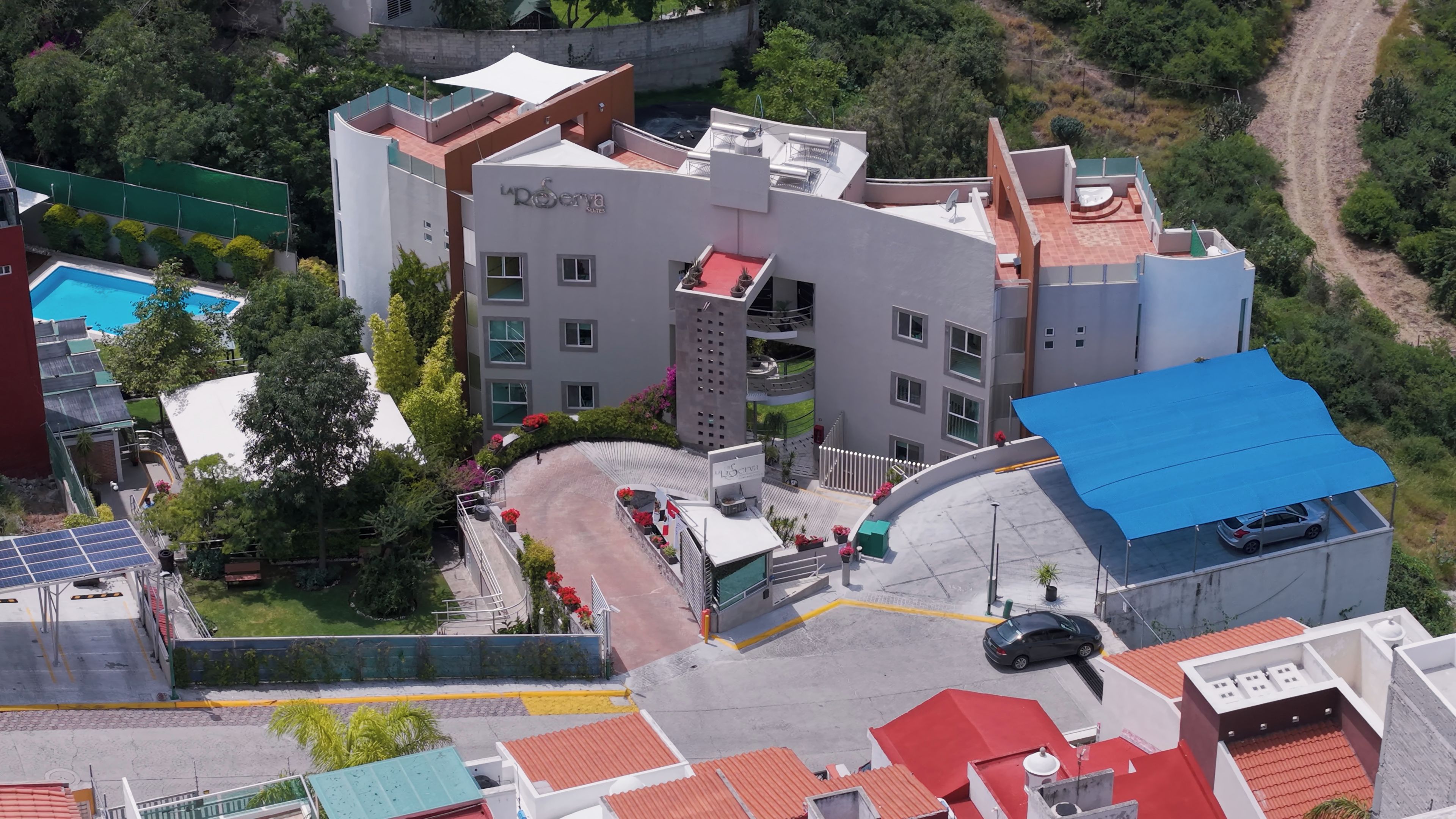 Un hotel de varios pisos con terraza en la azotea, piscina y estacionamiento.