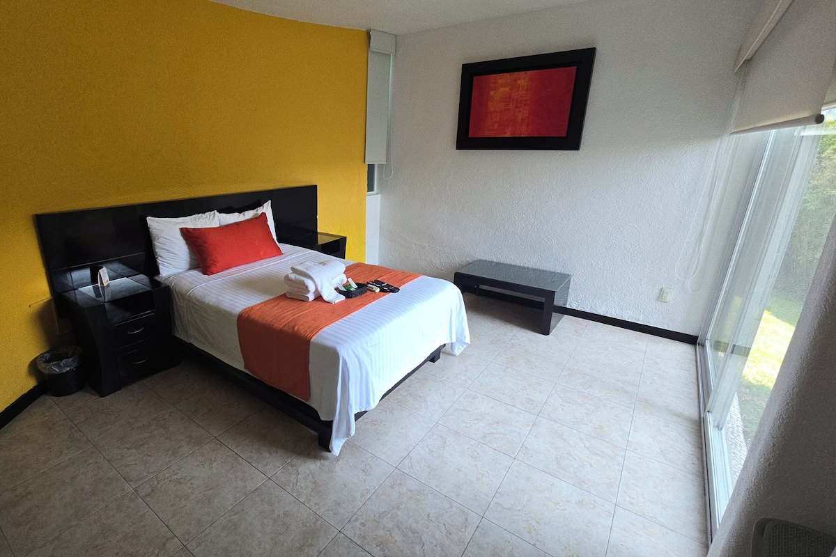 Una habitación de hotel con cama, mesitas de noche, un ventanal y una obra de arte colgada en la pared.