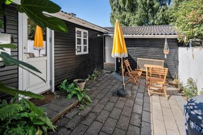 Eine Terrasse mit einem Holztisch und Stühlen, einem gelben Sonnenschirm und einem Blumentopf.