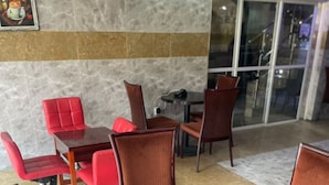 Un área de comedor con mesas y sillas redondas, un banco tapizado de color rojo y una puerta de cristal que da al exterior.