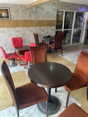 Un espace repas avec des tables et des chaises rondes, un banc rouge rembourré et une porte vitrée donnant sur l’extérieur.