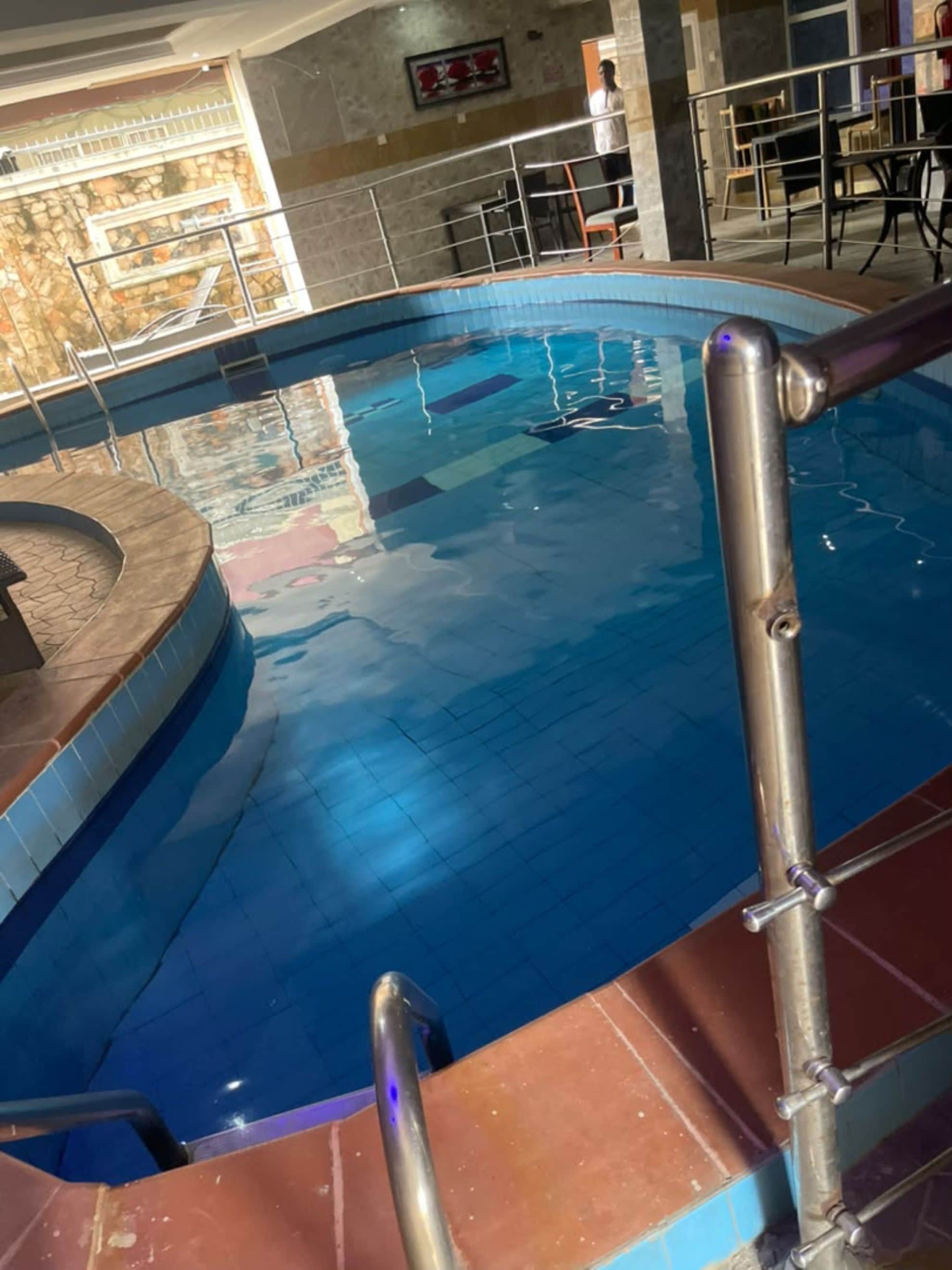 A swimming pool with a metal handrail and tiled steps leading into it.