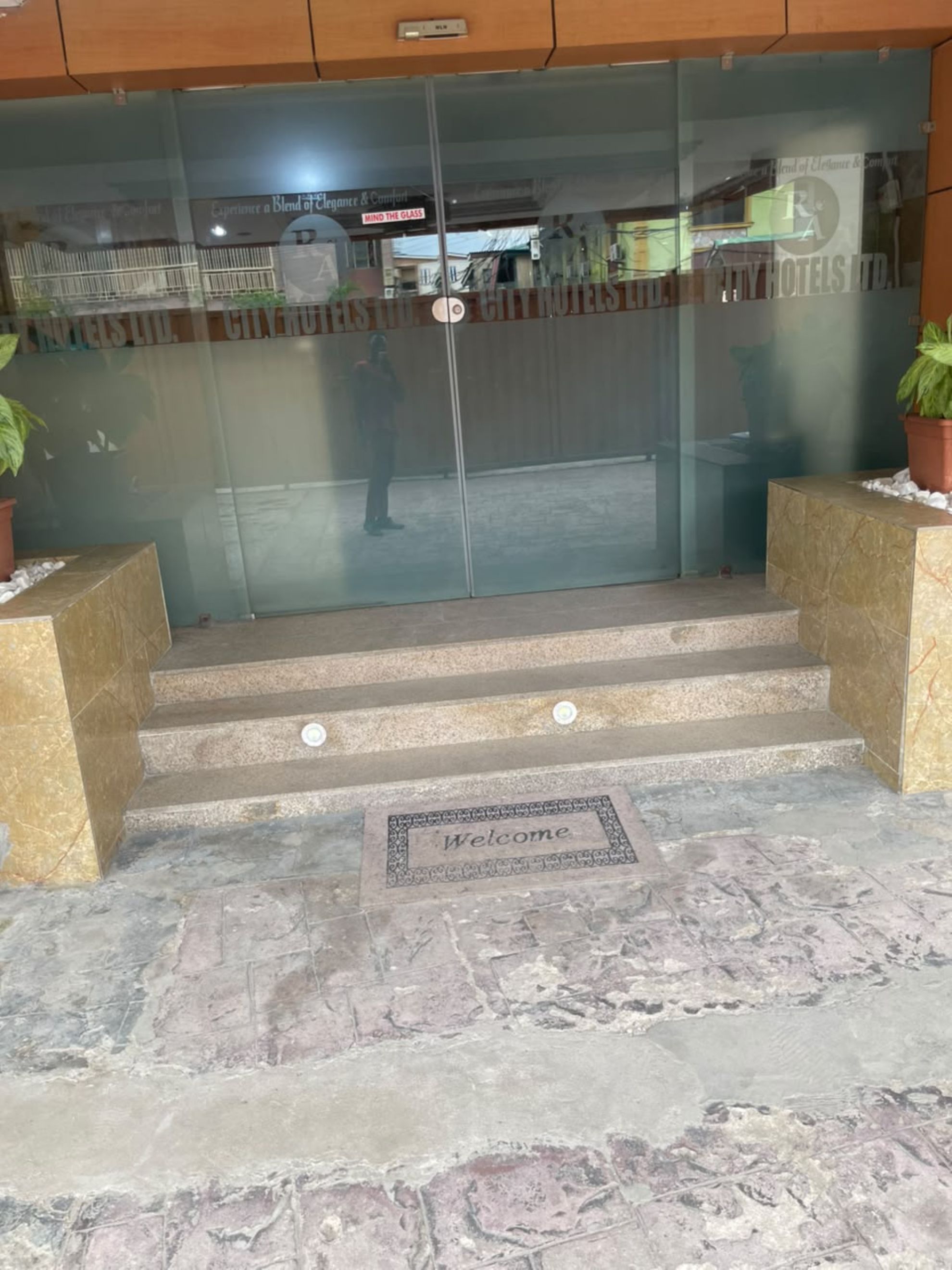 A hotel entrance with a glass door, a welcome mat, and a sign above the door.