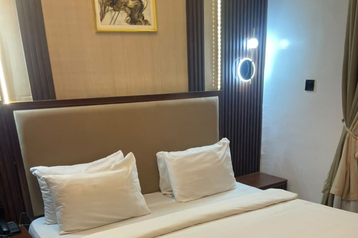 Une chambre d’hôtel avec un grand lit, deux oreillers, une table de chevet avec un téléphone et un luminaire fixé au mur.