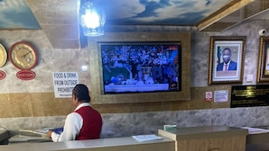 Una recepción con una pantalla de televisión mostrando un noticiero, un reloj y un cartel que indica que no se permite comida ni bebida de fuentes externas.