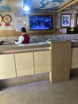 Un comptoir d’accueil est équipé d’un écran de télévision diffusant un bulletin d’information, d’une horloge et d’un panneau indiquant qu’il est interdit d’introduire de la nourriture ou des boissons provenant de l’extérieur.