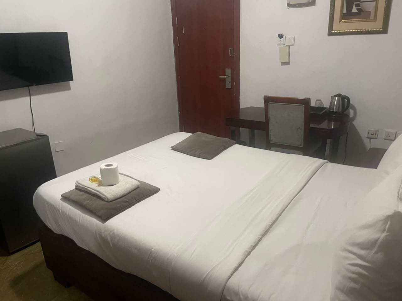 Een hotelkamer met een bed, een bureau, een stoel, een televisie en een deur.