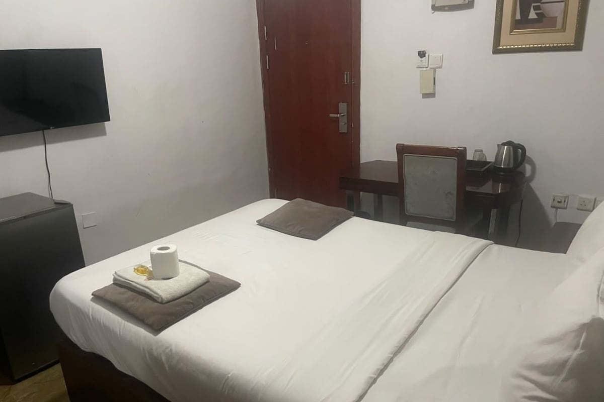 Une chambre d’hôtel avec un lit, un bureau, une chaise, une télévision et une porte.