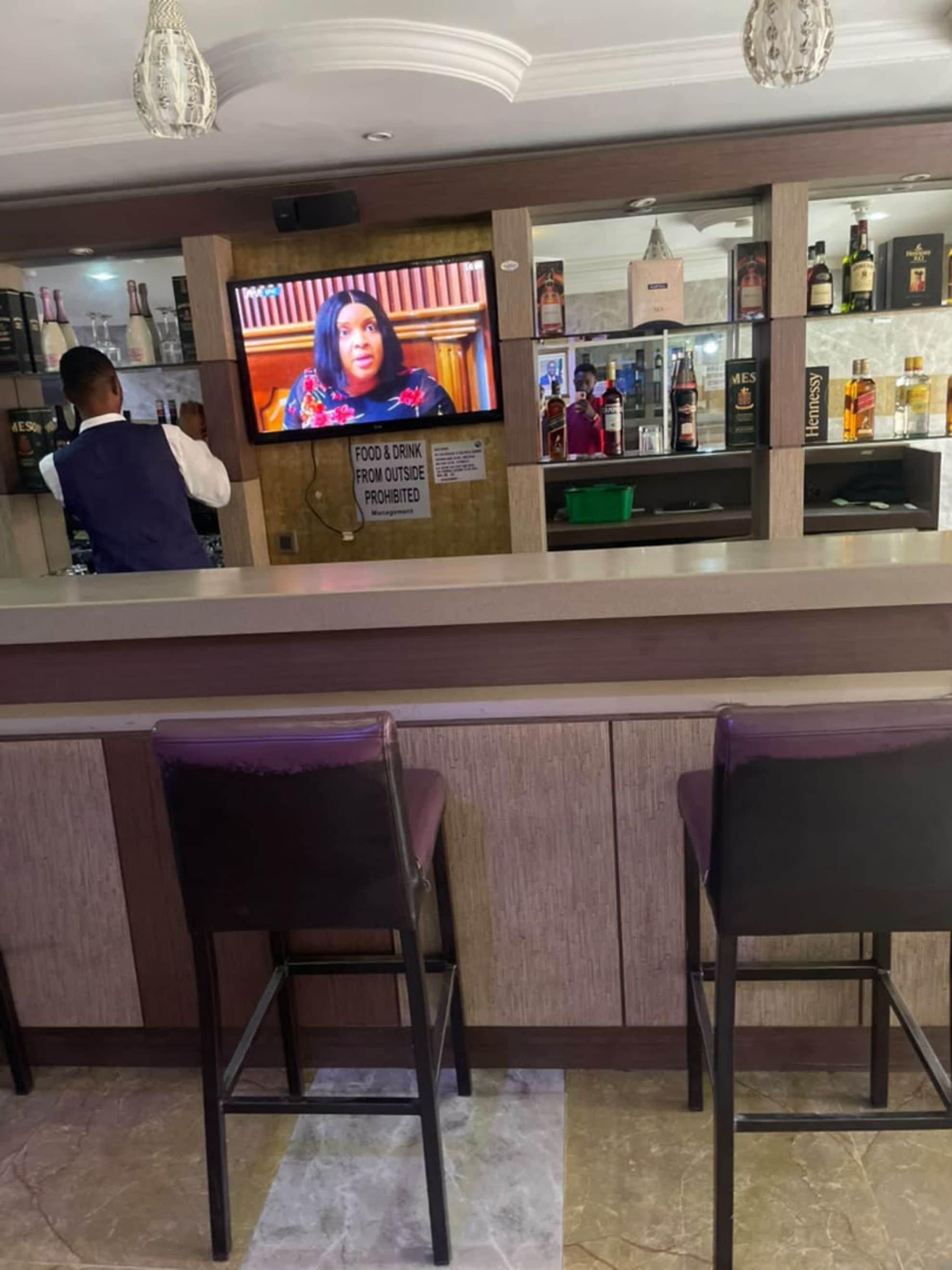 A bar area with a television screen, a sign prohibiting outside food and drink, and a variety of liquor bottles.