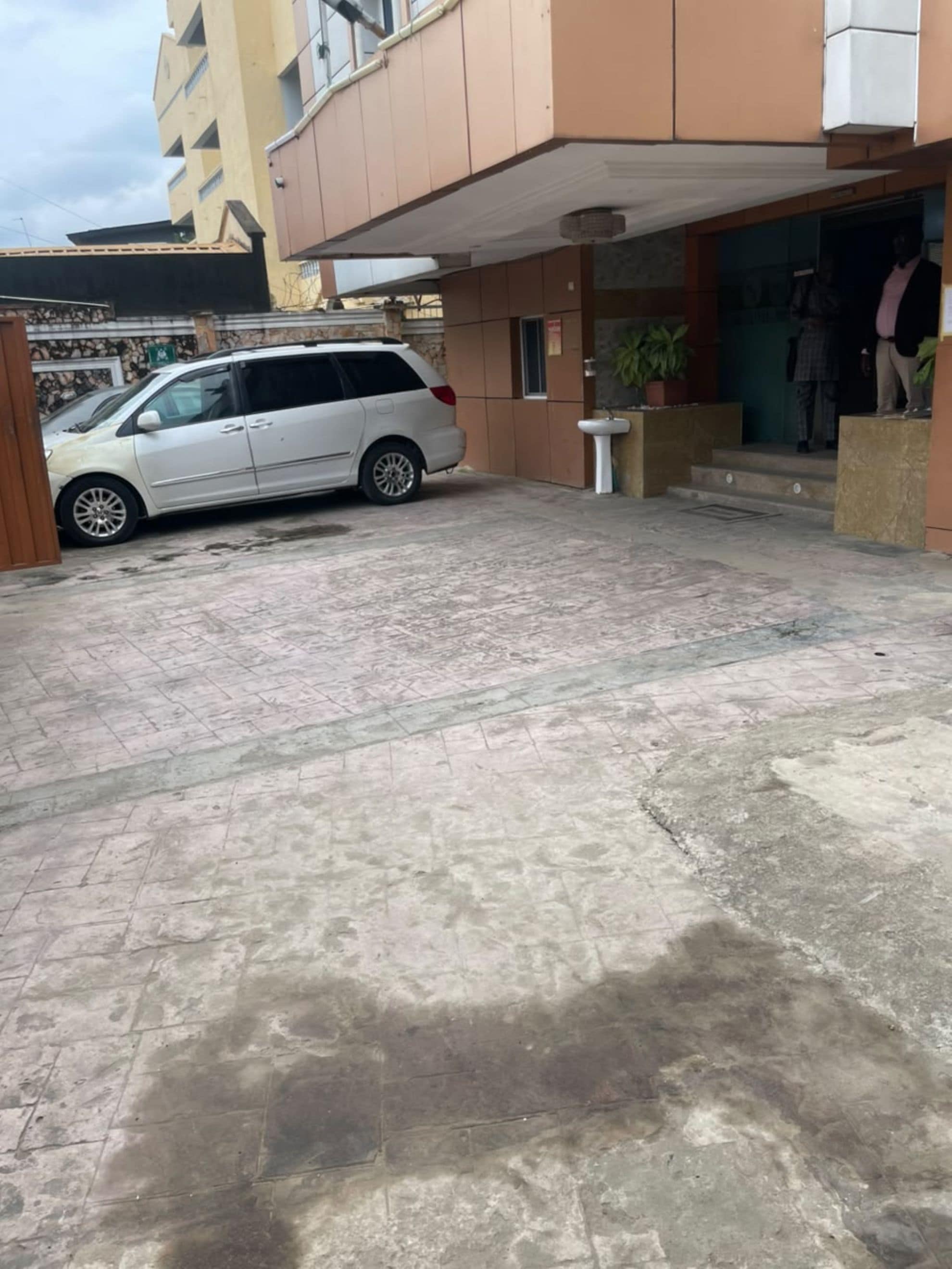 A building with a covered entrance, a white van parked in front, and a potted plant near the entrance.