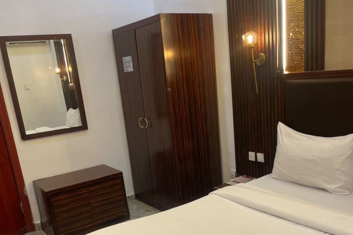 Une chambre d’hôtel comprenant un lit, une armoire, une commode, un miroir et un luminaire fixé au mur.