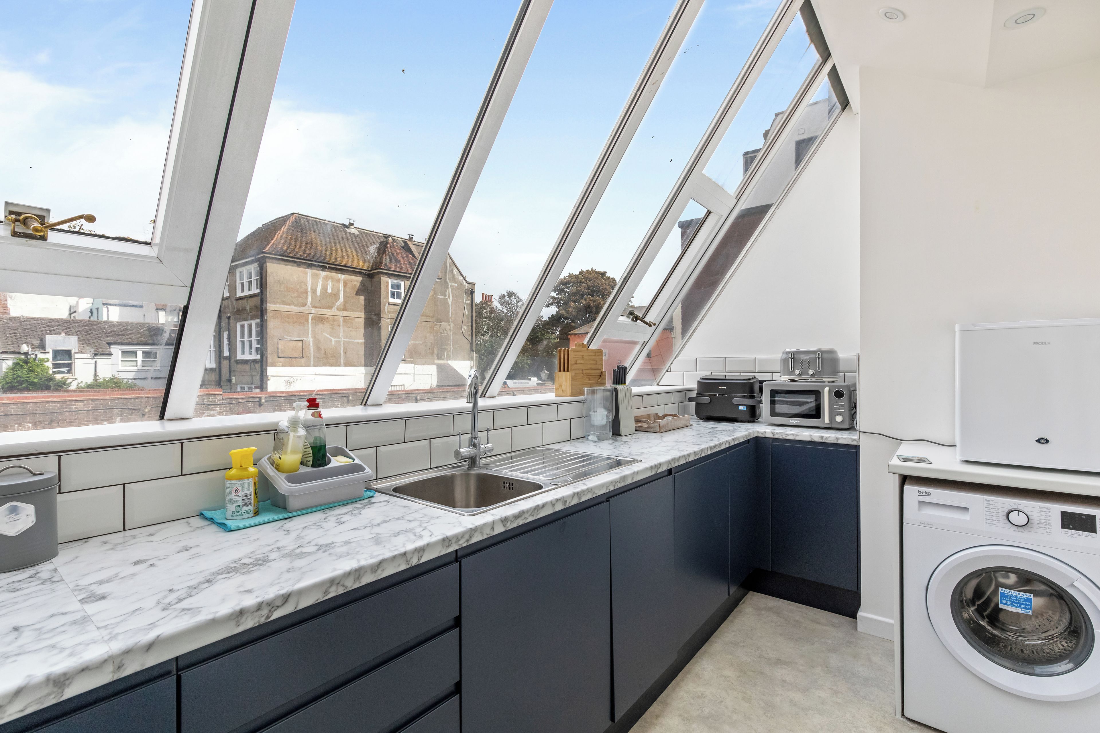 A modern kitchen with a built-in washing machine, a sink, and a window overlooking a residential area.