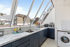 A modern kitchen with a built-in washing machine, a sink, and a window overlooking a residential area. - Stunning High-Spec 2-Bedroom Holiday Apartment in the Heart of Brighton. (Brighton and Hove)