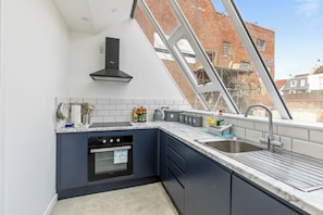 A modern kitchen with a built-in oven, a stainless steel sink, and a window overlooking a brick building. - Stunning High-Spec 2-Bedroom Holiday Apartment in the Heart of Brighton. (Brighton and Hove)