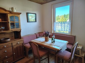 Ein gemütlicher Essbereich mit Holztisch und Bänken, einem Schrank mit Glastüren sowie einem Fenster mit Blick auf Grünflächen.