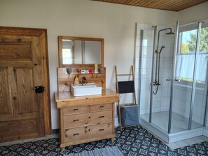 Ein Badezimmer mit Holzwaschtisch, Spiegel, Dusche mit Glastüren und fliesenbelagtem Boden.