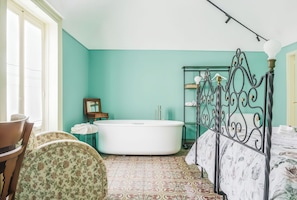 Un dormitorio con una bañera grande, una cama con colcha estampada de flores, una silla con diseño floral y un cabecero de metal.