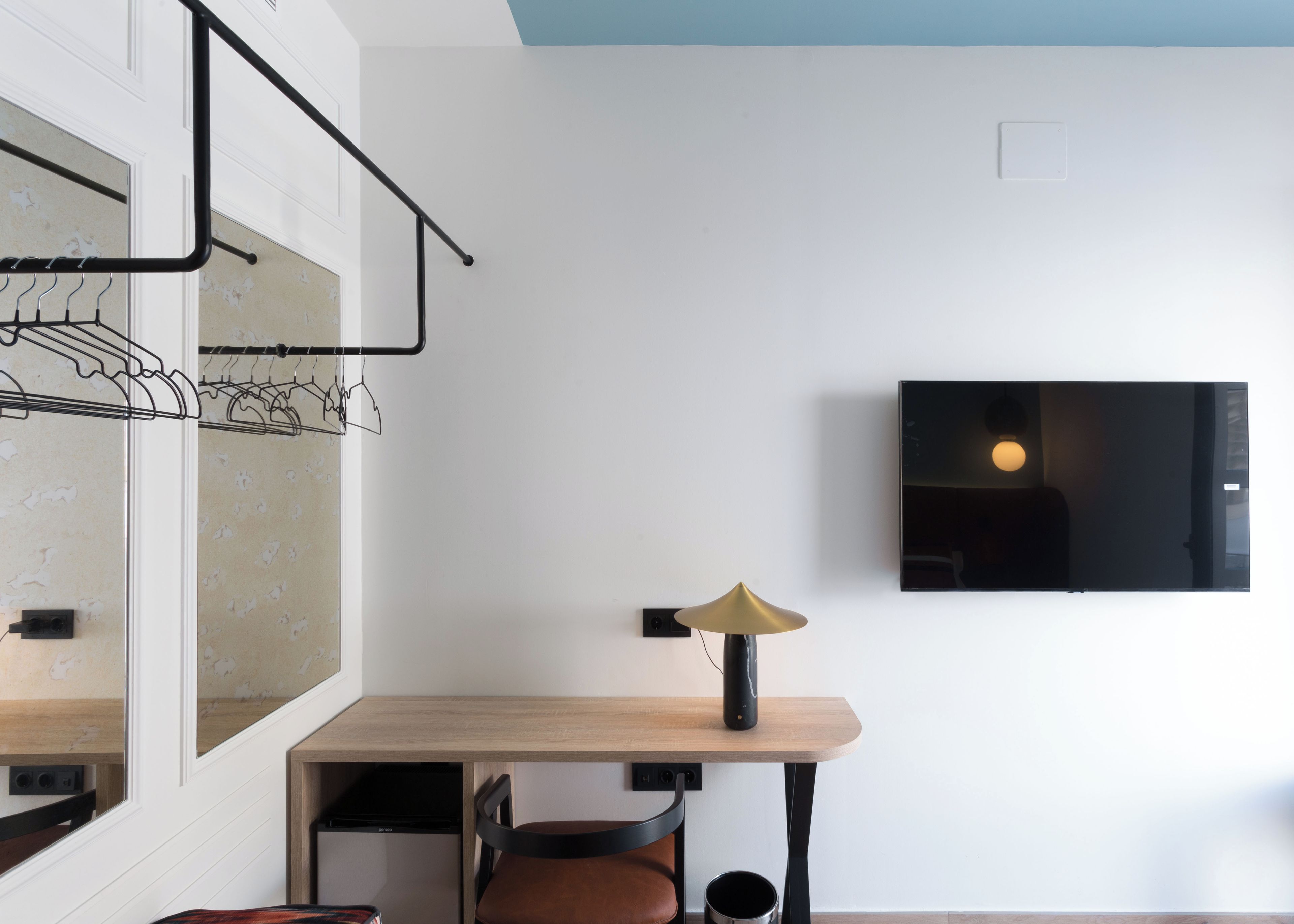 Una habitación moderna con un escritorio de madera, una silla, un perchero y un televisor montado.