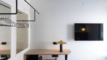 Una habitación moderna con un escritorio de madera, una silla, un perchero y un televisor montado.