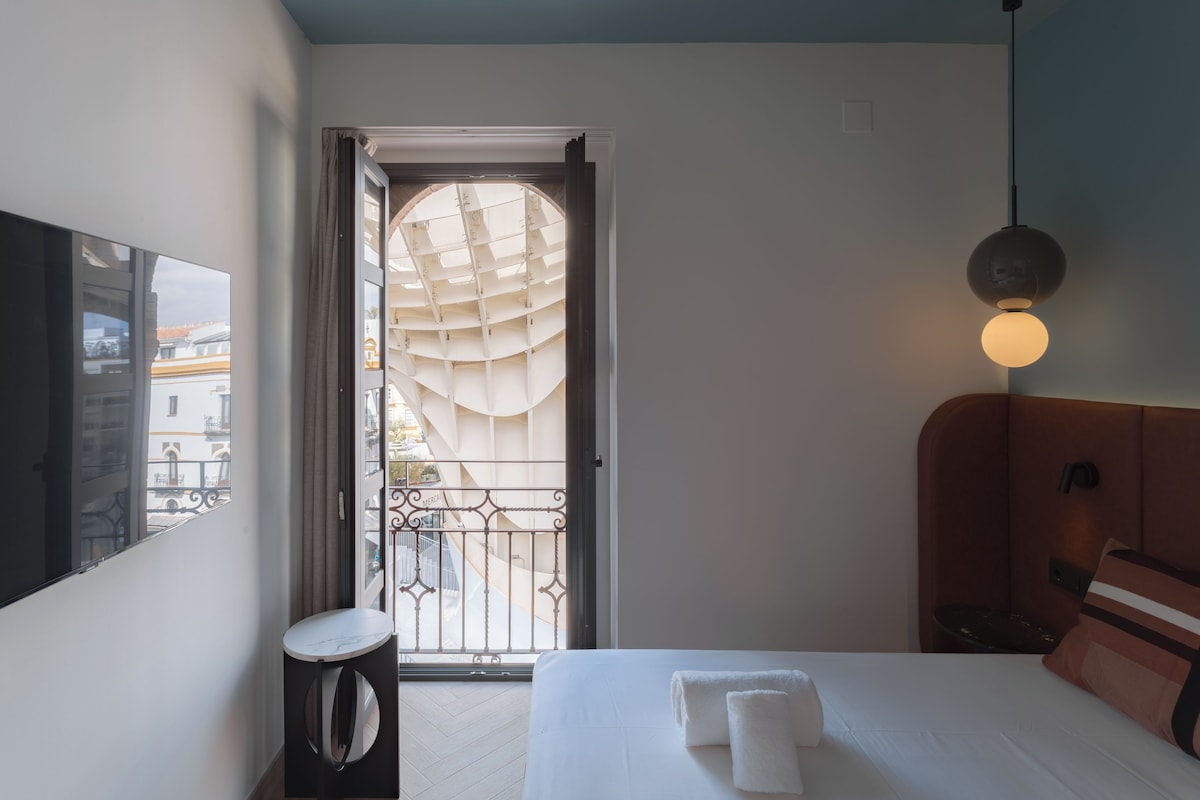 Quarto de hotel com uma cama, mesa de cabeceira, abajur e vista para o exterior pela janela.