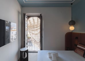 Quarto de hotel com uma cama, mesa de cabeceira, abajur e vista para o exterior pela janela.