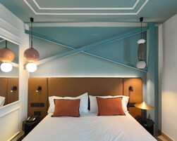 Une chambre d’hôtel équipée d’un lit, de tables de chevet, d’un téléphone et de luminaires suspendus.
