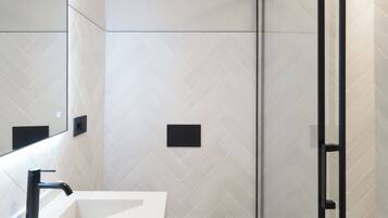 Un baño moderno con lavamanos, inodoro y zona de ducha blancos.