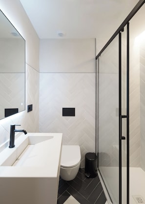 Ein modernes Badezimmer mit Waschbecken, Toilette und Duschbereich, alles in Weiß.