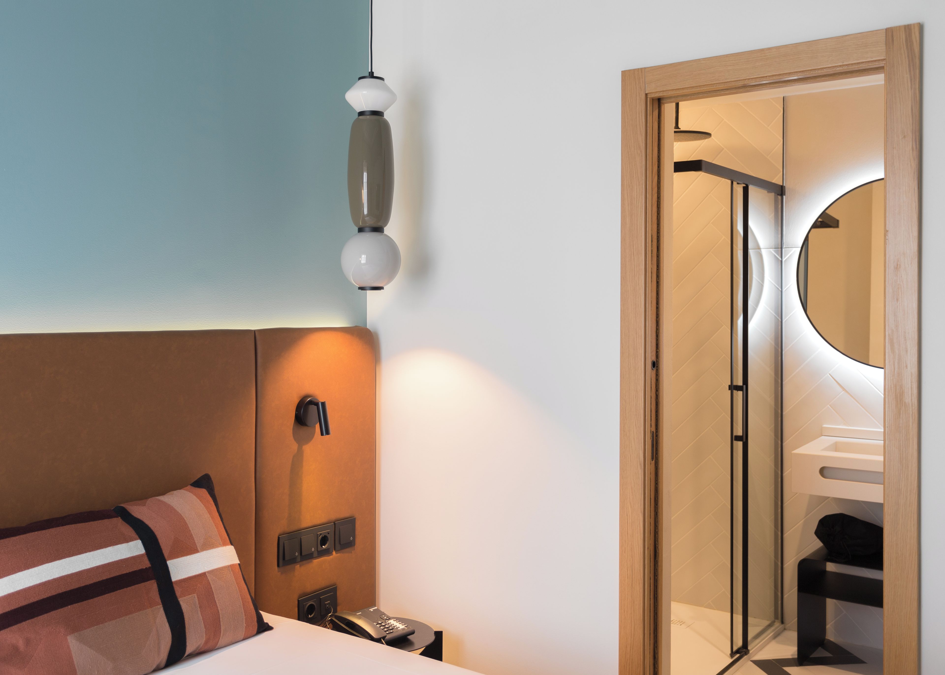 Habitación de hotel con cama, mesita de noche con teléfono, lámpara de pared y espejo con marco de madera.