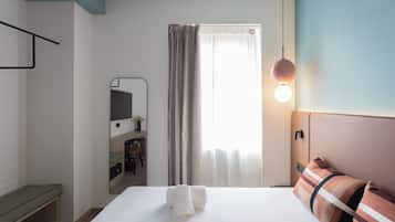 Ein Hotelzimmer mit einem Bett, einem Nachttisch, einem Spiegel, einem Schreibtisch mit Stuhl, einem Fenster mit Vorhängen und einer Wandleuchte.