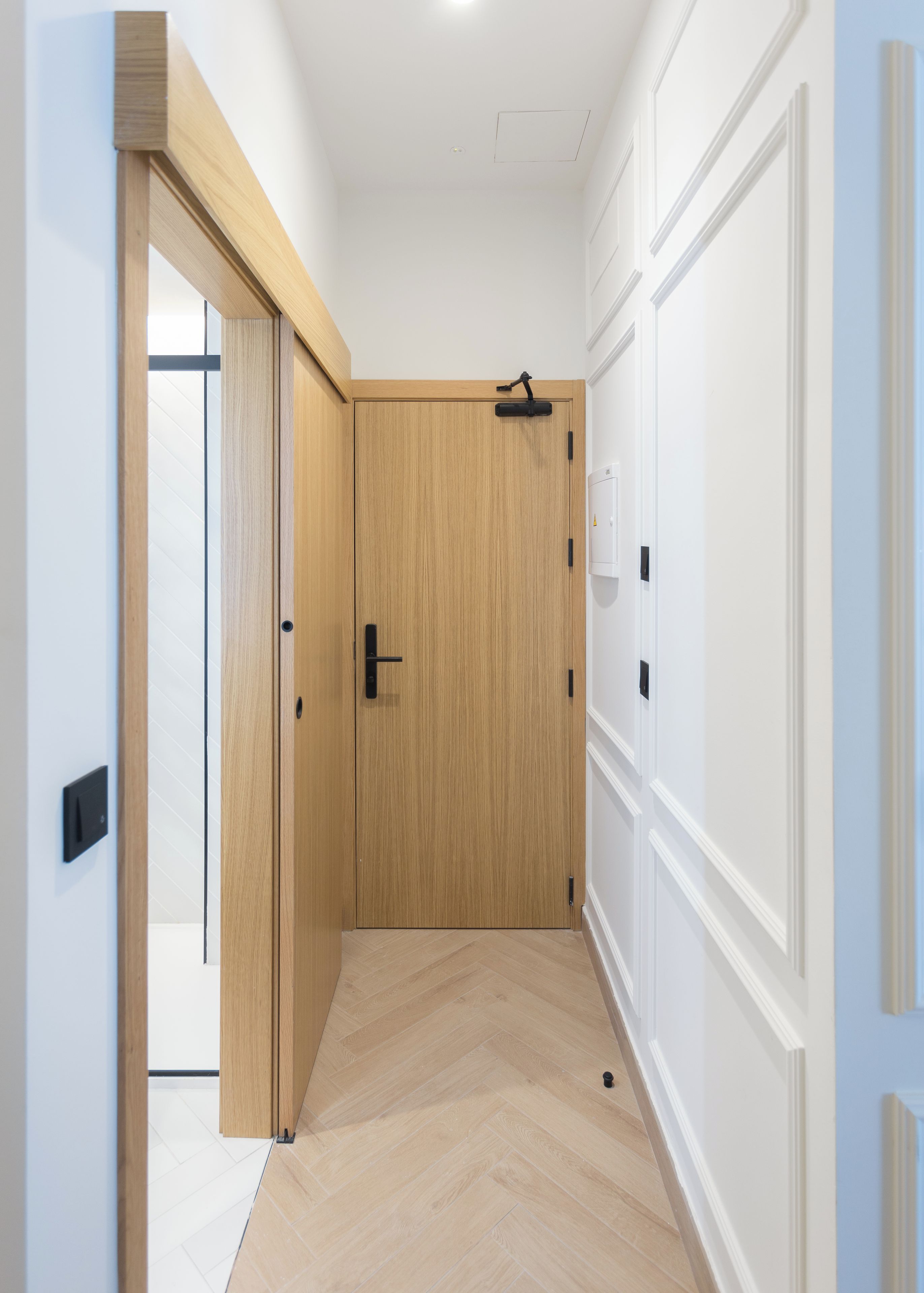 A hallway with a wooden door, a light switch, and a thermostat on the wall.