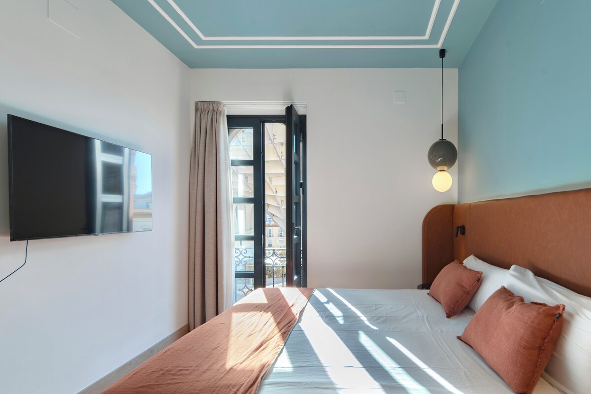 Un dormitorio con cama, televisor, ventana con cortinas e iluminación en el techo.
