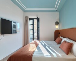 A bedroom with a bed, a TV, a window with curtains, and a ceiling light.