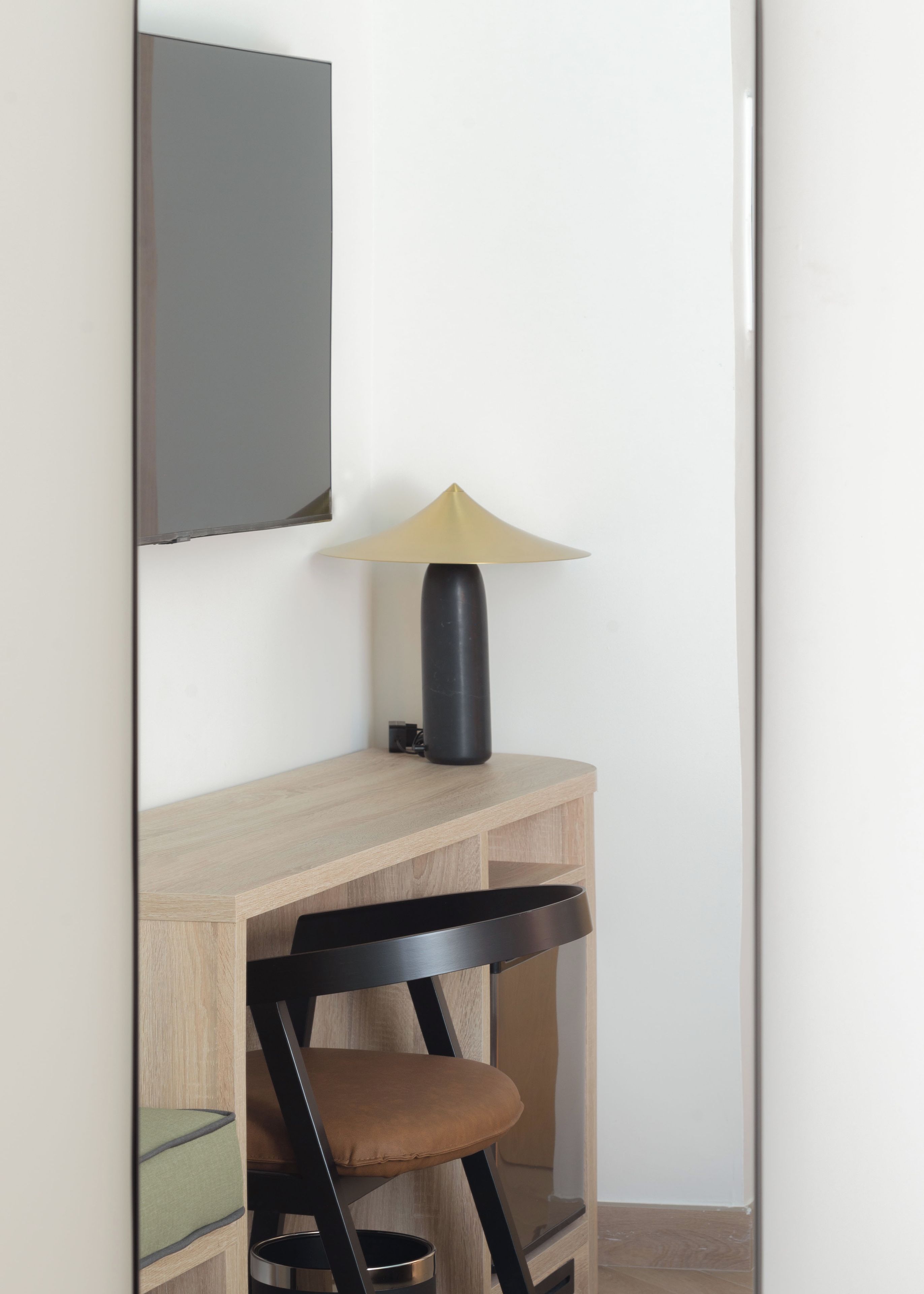 A desk with a lamp, a chair, and a television mounted on the wall.