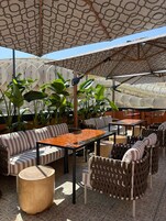 Un'area salotto all'aperto con divani a righe, tavoli tondi e un soffitto decorato.