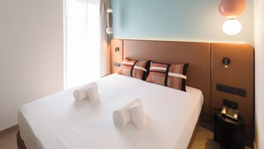 A hotel room with a large bed, a bedside table with a phone, and a wall-mounted light fixture. - Casa Candela Sevilla (Sevilla)